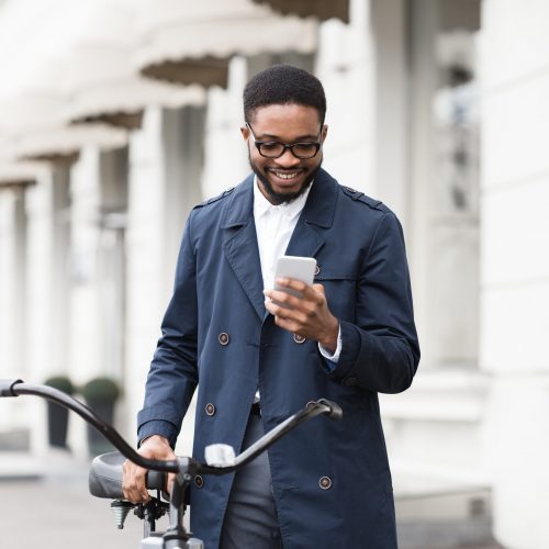Way to work. Man texting on phone, standing with bike